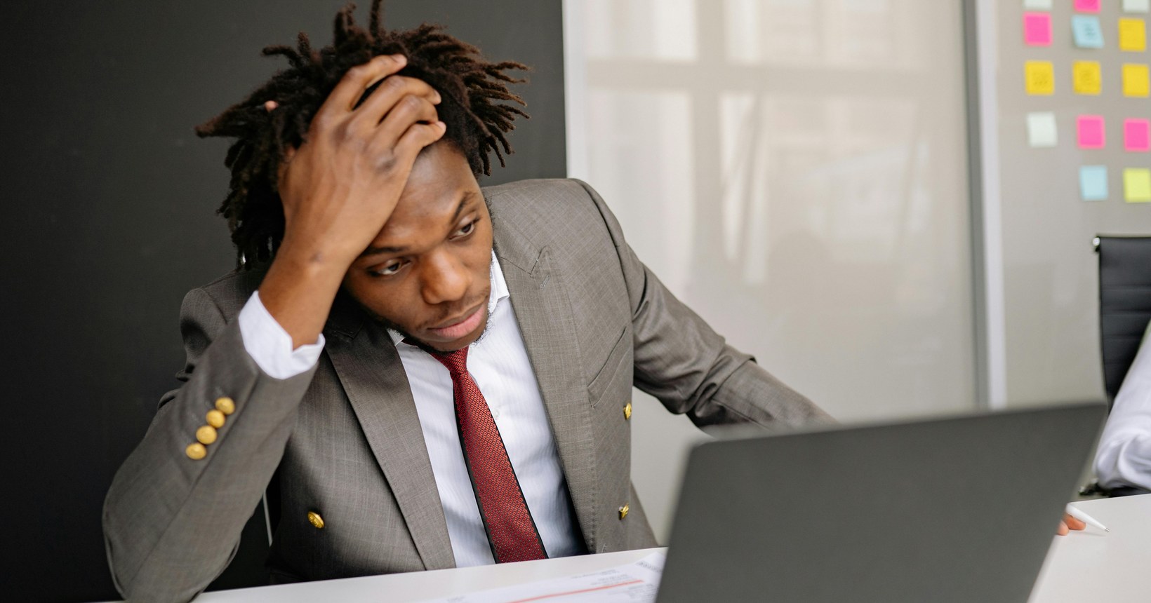 Man in a suit holding his head in his hands while staring at a laptop, conveying anxiety about AI job displacement