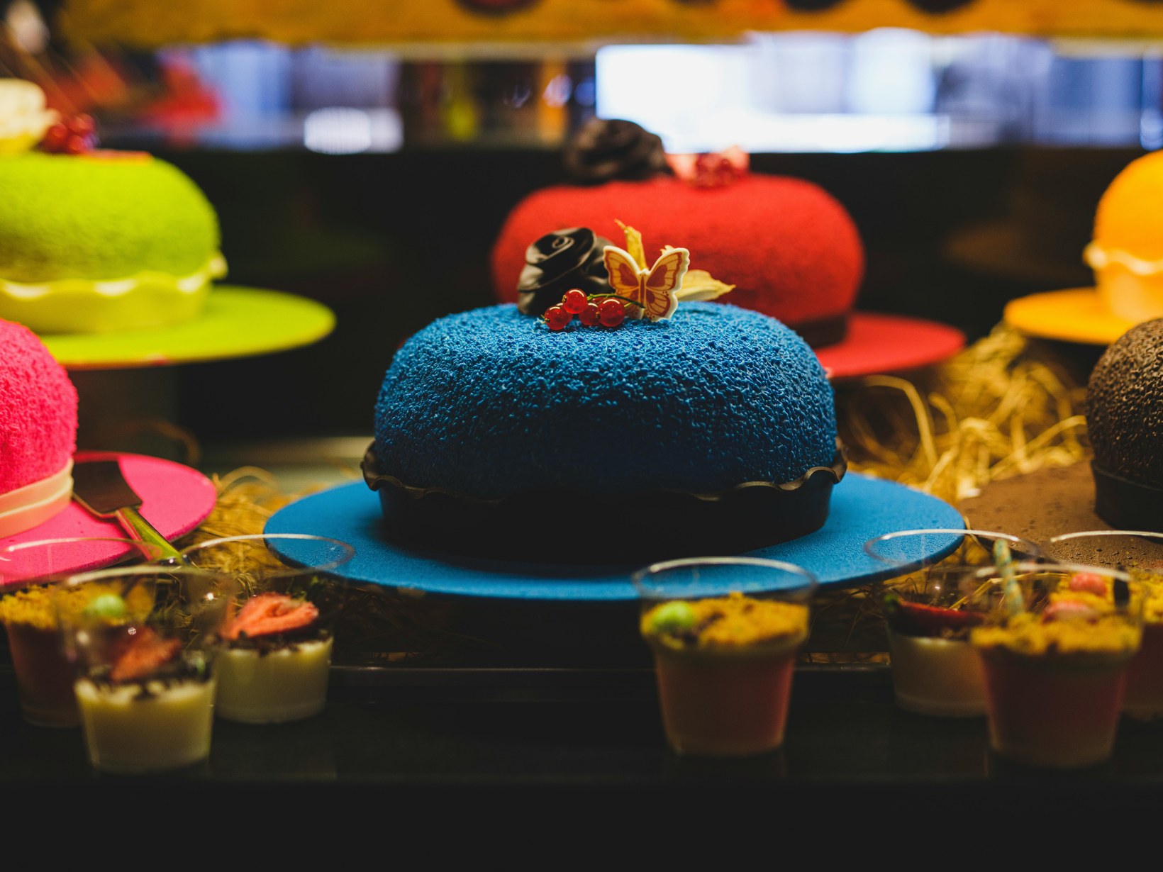 Display case showing a striking blue velvet cake surrounded by colourful desserts in a patisserie