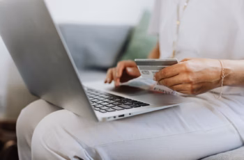 A person sitting on a sofa holding a credit card while checking out on a laptop