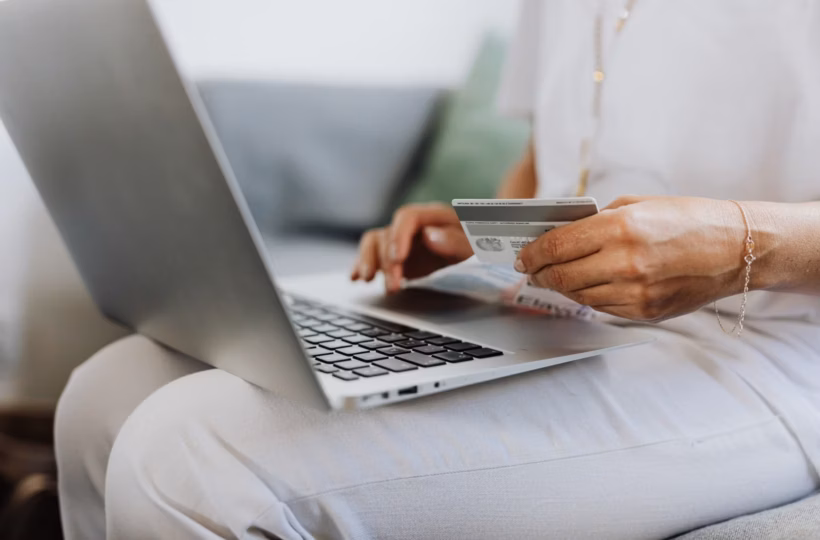 A person sitting on a sofa holding a credit card while checking out on a laptop