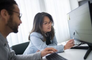 Woman pointing at a row of data on a computer monitor while a colleague looks on