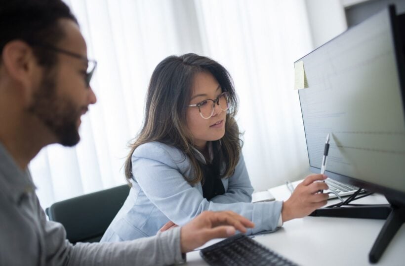 Woman pointing at a row of data on a computer monitor while a colleague looks on