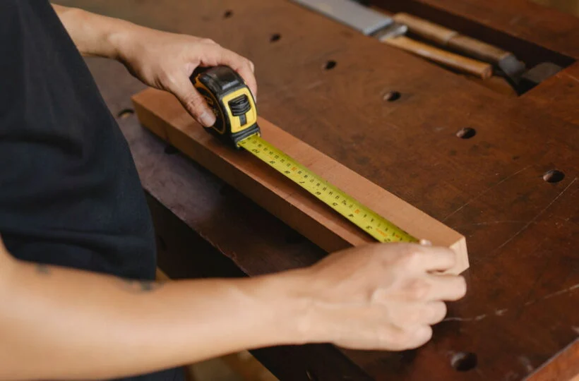 A maker measuring a length of timber with a tape measure