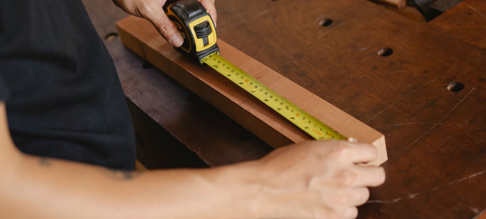 A maker measuring a length of timber with a tape measure, the kind of made-to-measure product usually sold by quote